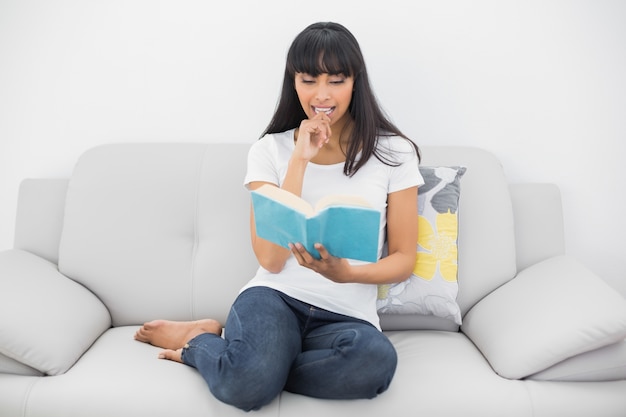 Foto mujer de pelo oscura tranquila leyendo un libro sentado en el sofá