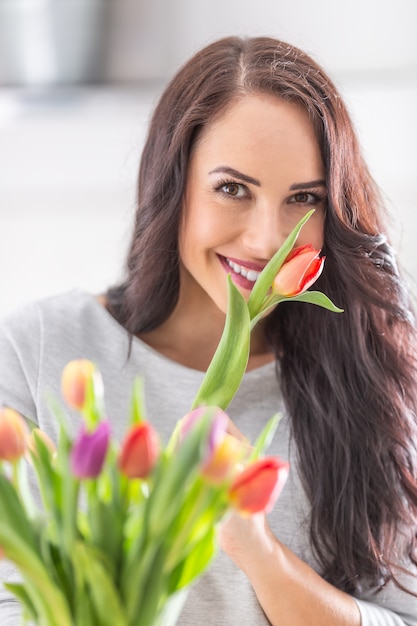 Mujer de pelo oscuro que huele el aroma encantador de los tulipanes coloridos de la primavera fresca.