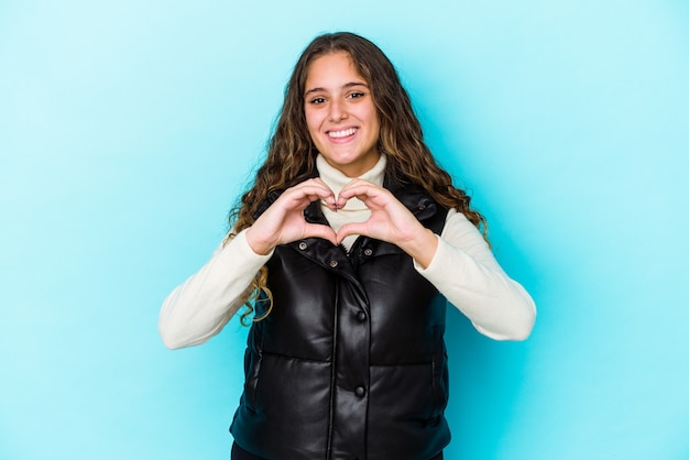 Mujer de pelo rizado caucásico joven aislada sonriendo y mostrando una forma de corazón con las manos.