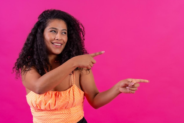 Mujer de pelo rizado con ropa de verano de fondo rosa apuntando a la foto de estudio correcta