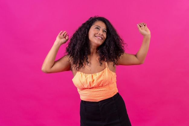 Mujer de pelo rizado con ropa de verano en una foto de estudio de baile de fondo rosa