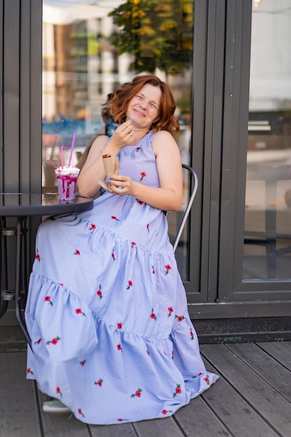 mujer con pelo rojo en un café bebe un cóctel de verano, feliz, ríe, sonríe.