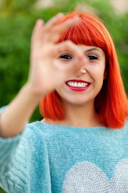 Mujer de pelo rojo diciendo Ok con su mano en un parque