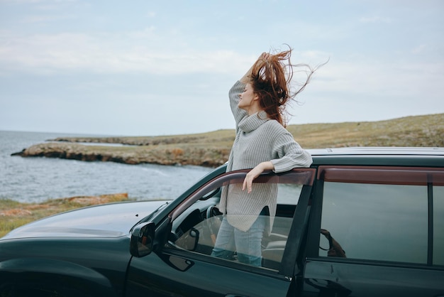 Mujer con pelo rojo en un suéter cerca del coche naturaleza mujer relajante