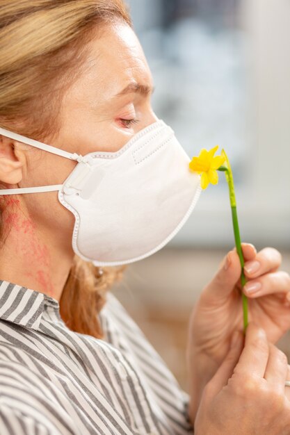 Mujer de pelo rubio con máscara protectora mientras tiene alergia a las flores