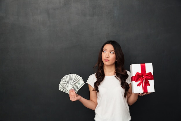 Mujer de pensamiento joven asiática con dinero y caja de regalo