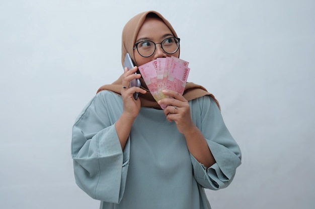 Mujer pensando y hablando por teléfono mientras sostiene dinero indonesio