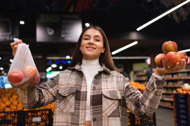 Foto la mujer está pensando si tomar manzanas en una bolsa de plástico o prescindir de ellas