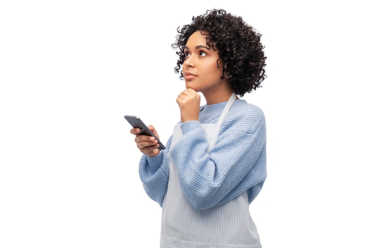 Foto mujer pensante en delantal con teléfono inteligente