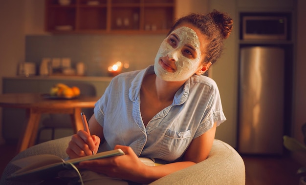 Mujer pensante escribiendo ideas en un libro haciendo mascarilla facial de belleza para el cuidado de la piel y el cuidado personal facial sentada en la sala de estar en casa Mujer creativa que parece pensativa mientras planifica la rutina en el cuaderno