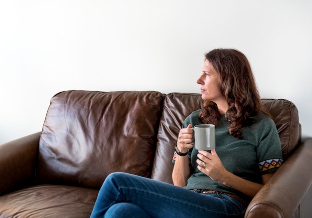 Mujer pensativa bebiendo té o café sentado en un sofá acogedor