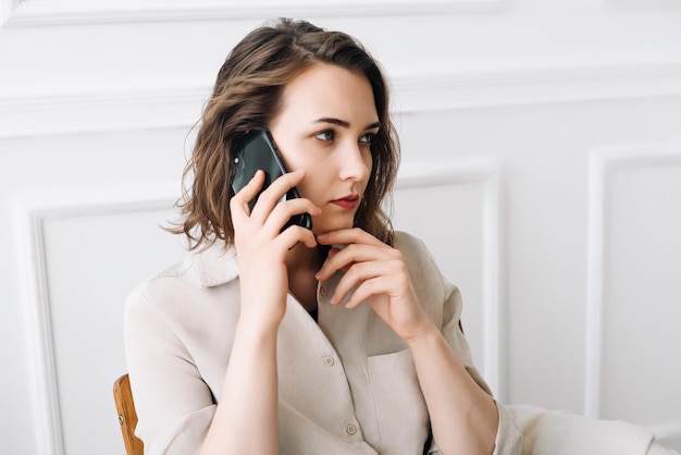 Una mujer pensativa de la generación del milenio hace una llamada telefónica habla intensamente y contemplativamente sentada en una mesa