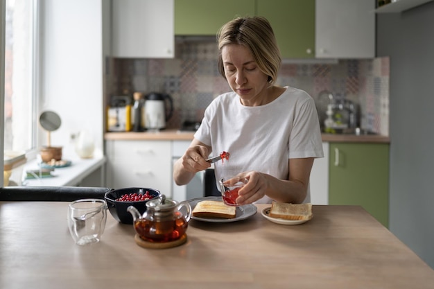 Una mujer pensativa de mediana edad se sienta sola en la mesa de la cocina comiendo comida saludable por la mañana