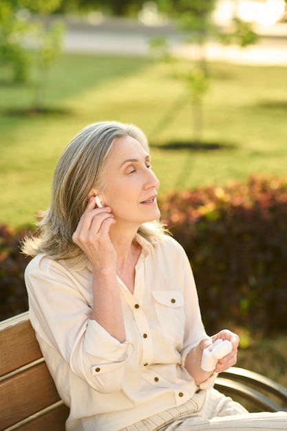 Mujer pensativa poniendo auriculares inalámbricos