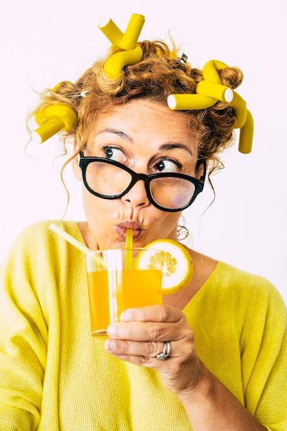 Mujer pensativa con rulos bebiendo un vaso de jugo Mujer joven aplica rulos en el cabello