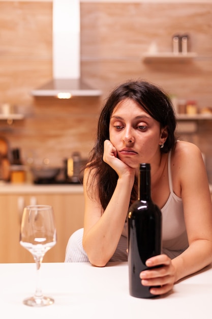Mujer pensativa sosteniendo una botella de vino deprimida debido a la ruptura.