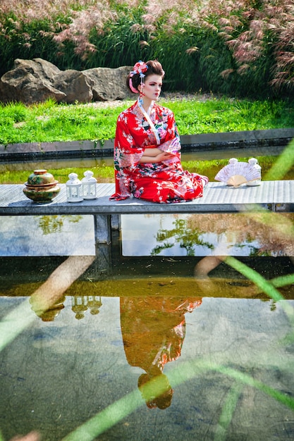 Mujer pensativa en traje de geisha en el jardín en el puente