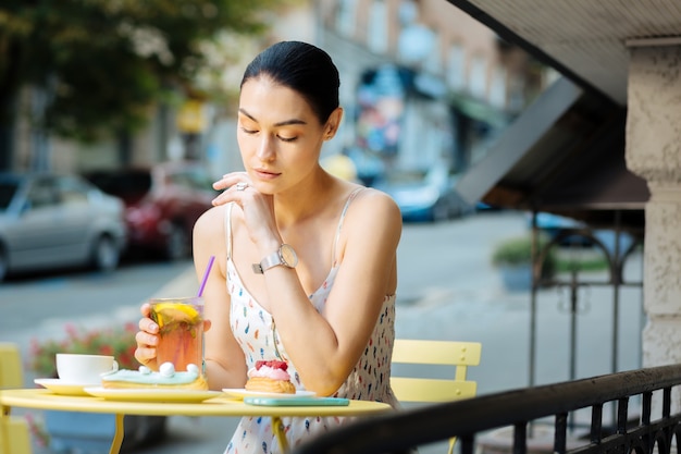 Mujer pensativa. Tranquila joven visitando un café de la calle y mirando pensativamente la limonada