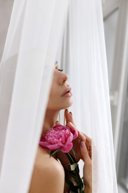 Mujer con una peonía en un primer plano de fondo blanco tierno. belleza