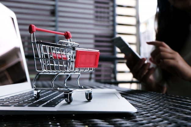 Mujer y pequeño carro de compras con ordenador portátil para el concepto de compras en línea por Internet