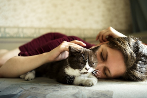 Foto mujer y un pequeño gatito británico blanco y negro están tumbados en el sofá