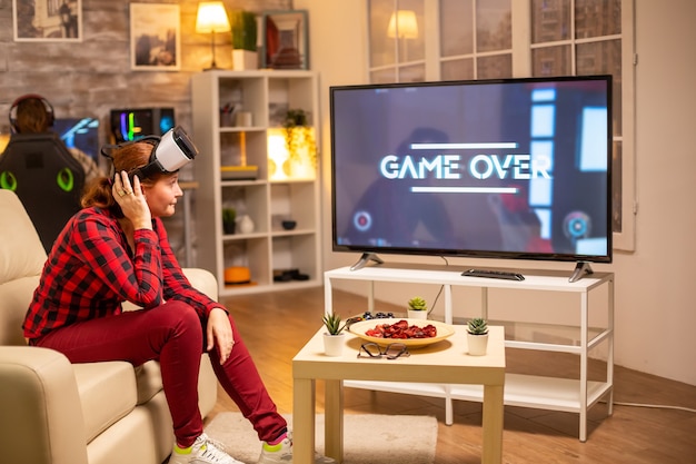 Mujer perdiendo en videojuegos mientras juega con casco de realidad virtual a altas horas de la noche en la sala de estar