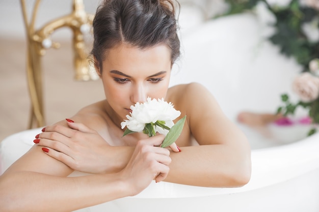 Mujer perfecta bañándose con flores y leche