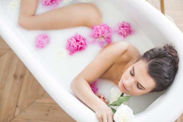 Mujer perfecta bañándose con flores y leche