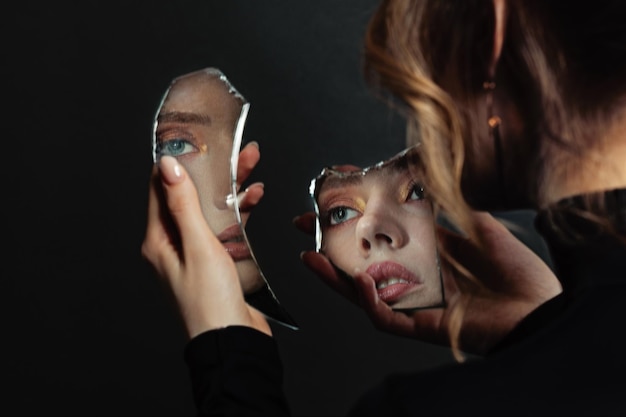 La mujer perfecta mirando el espejo de autoimagen roto sobre un fondo negro