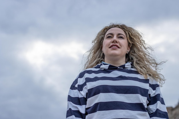 Una mujer de perfil en un día de otoño con un abrigo y con los ojos cerrados mientras el viento sopla en su rostro al aire libre