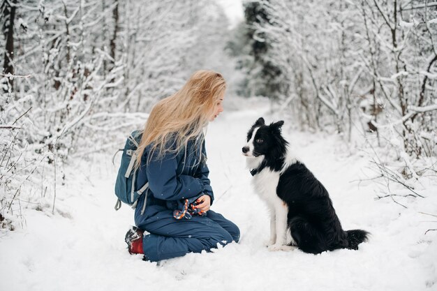 Mujer con un perro border collie blanco y negro en el bosque nevado