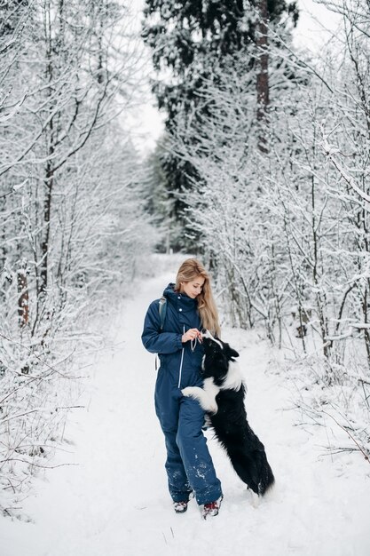 Mujer con un perro border collie en el bosque nevado