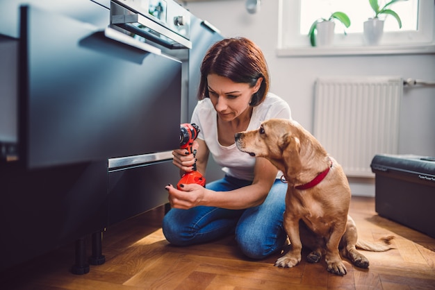 Mujer con perro construyendo cocina y usando un taladro inalámbrico