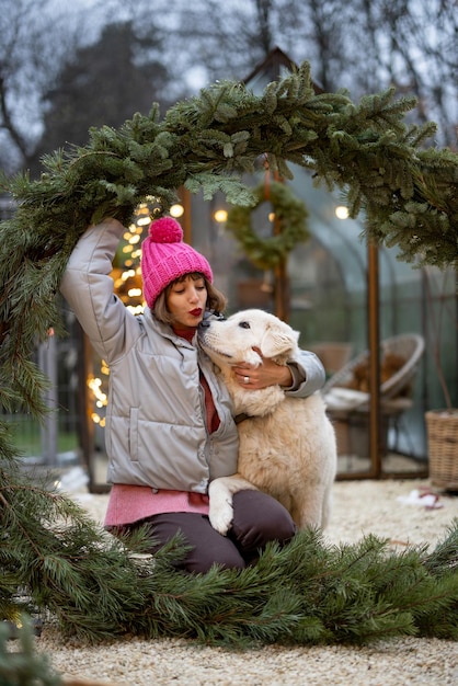Mujer con un perro en corona de navidad en el patio trasero