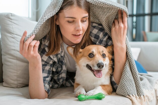 Foto mujer con perro debajo de la manta en el sofá