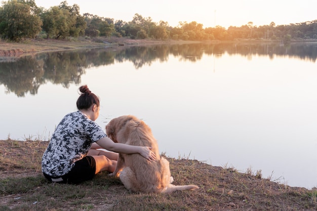 Mujer y perro Golden retriever sentado cerca de río o lago