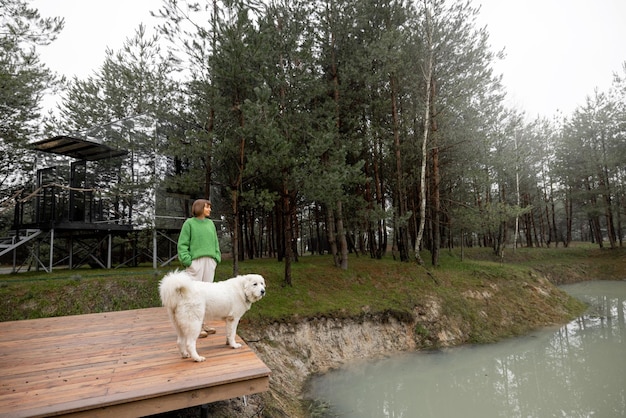 Mujer con perro en el muelle cerca del lago en el bosque de pinos