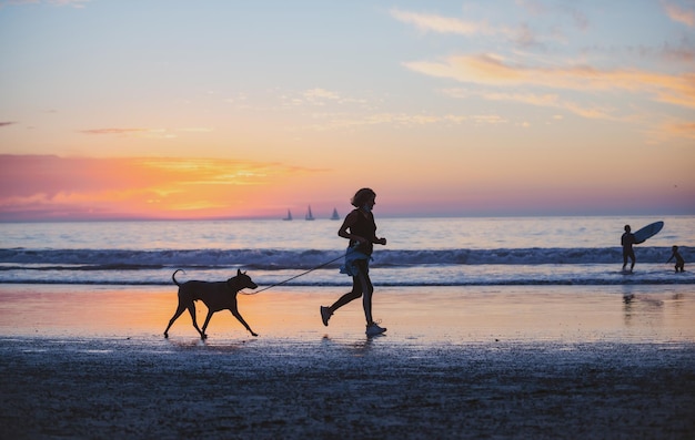 Mujer con perro en la playa sobre fondo dorado atardecer océano marino