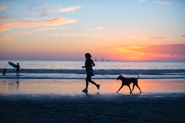 Mujer con perro en la playa sobre fondo dorado atardecer océano marino