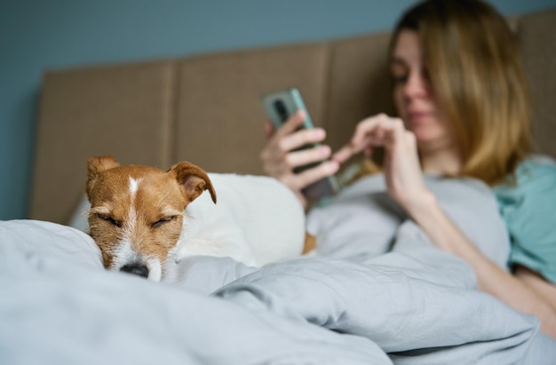 Mujer con perro relajándose en la cama usa smartphone