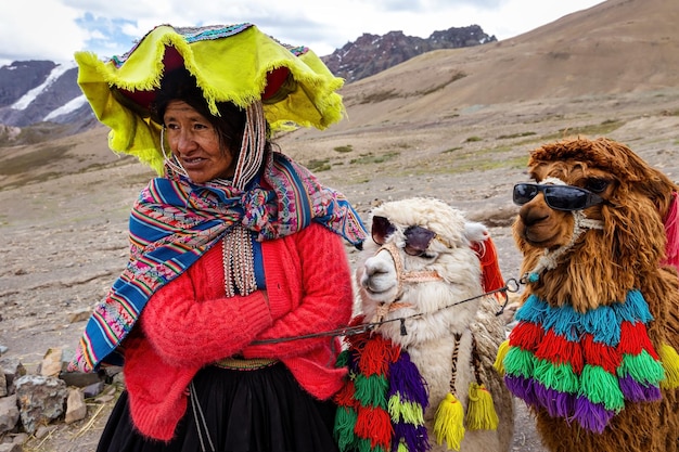 Mujer peruana con ropa tradicional con dos llamas en el fondo de las montañas