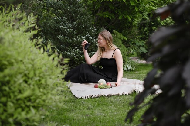 Mujer en picnic en el jardín verde en la manta alegremente mujer pasa el tiempo al aire libre comiendo verano