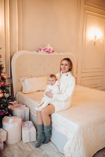 Mujer de pie con bebé cerca de árbol de Navidad.