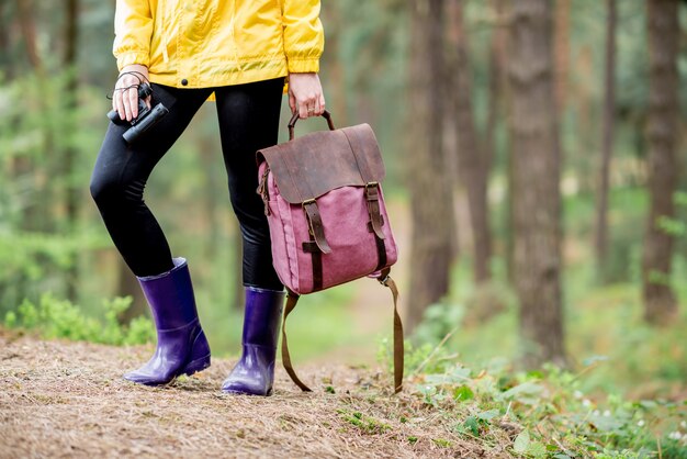 Mujer de pie con botas de goma con binoculares y mochila en el bosque verde. Vista cercana de las piernas