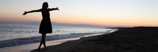 Mujer de pie con los brazos abiertos en la orilla del mar al atardecer