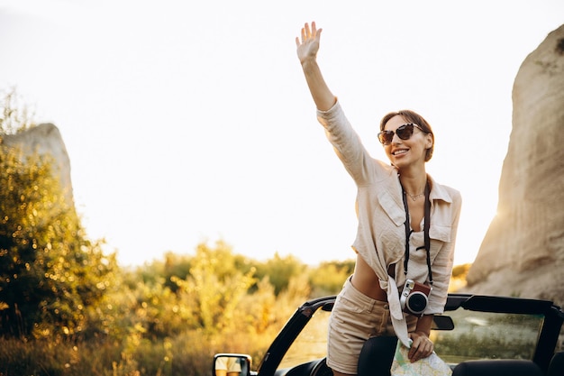 Mujer de pie en cabriolet en la puesta de sol de montaña con mapa y cámara