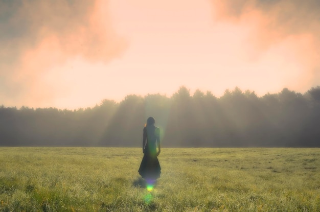 Foto mujer de pie en un campo de hierba contra un cielo nublado durante la puesta de sol