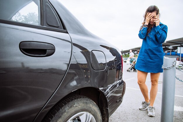 Foto mujer de pie cerca de un auto rasgado llama a ayuda seguro de coche