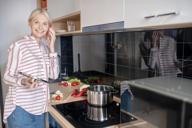 Mujer de pie cerca de la estufa en la cocina y hablando por teléfono