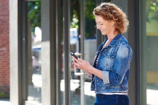 Mujer de pie en la ciudad con teléfono móvil con auriculares